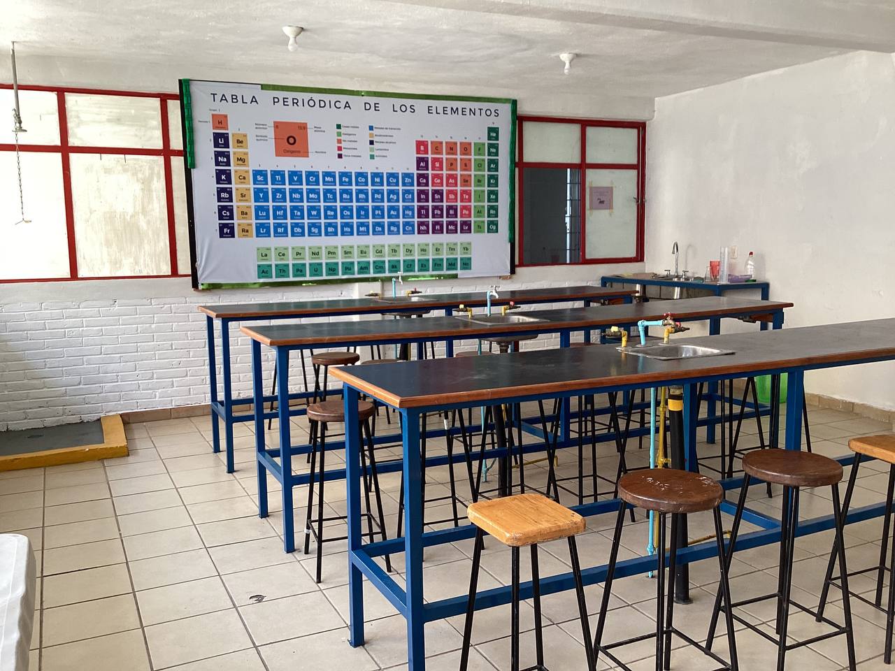 Laboratorio escolar con mesas de trabajo y tabla periódica
